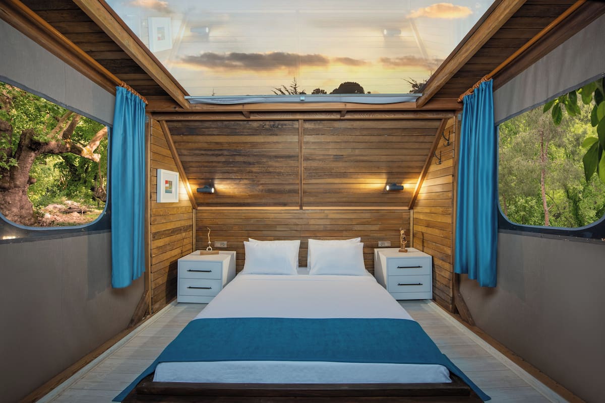 A bedroom with a wooden ceiling, a large bed, two bedside tables, and curtains on the windows.