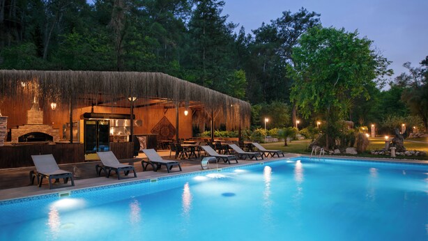 A swimming pool with lounge chairs and a thatched-roof structure. - YUSALİS GARDEN HOTEL (Kumluca)