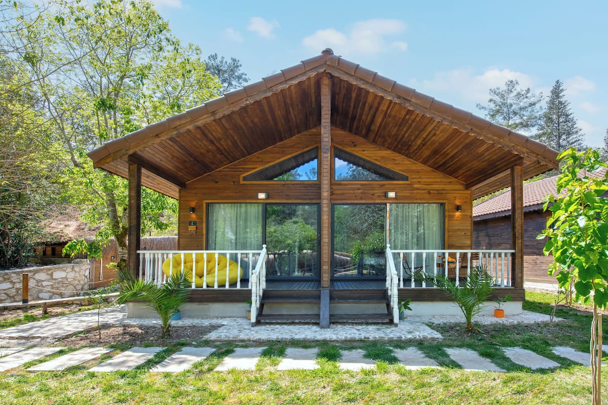 A wooden pavilion with a sloped roof, large glass doors, and a white railing.