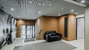 Um lobby moderno com um sofá de couro preto, uma parede de tijolos e um teto com padrão quadriculado.