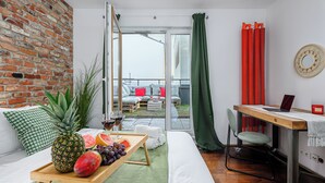 Uma sala de estar moderna com parede de tijolos, um sofá com almofadas estampadas, uma mesa de jantar com bandeja de frutas e um laptop em uma escrivaninha.