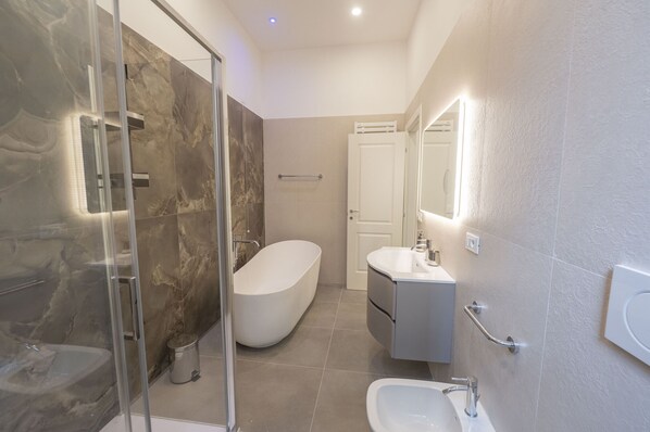 A modern bathroom with a glass-enclosed shower, a freestanding bathtub, a vanity with a mirror, and a toilet.