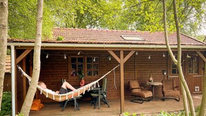 Una cabaña de madera con porche, una hamaca y mobiliario para exterior.