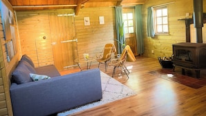 Interior acogedor de una cabaña con techo de madera, un sofá, una mesa con sillas, chimenea y una ventana con cortinas.