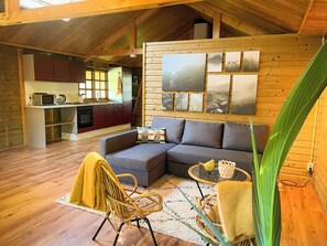 A cozy cabin interior with a dining area, kitchen, and a living room with a sofa and a chair. - Lodge The Kingfisher at Bolmeer lodges (Zevenhuizen)
