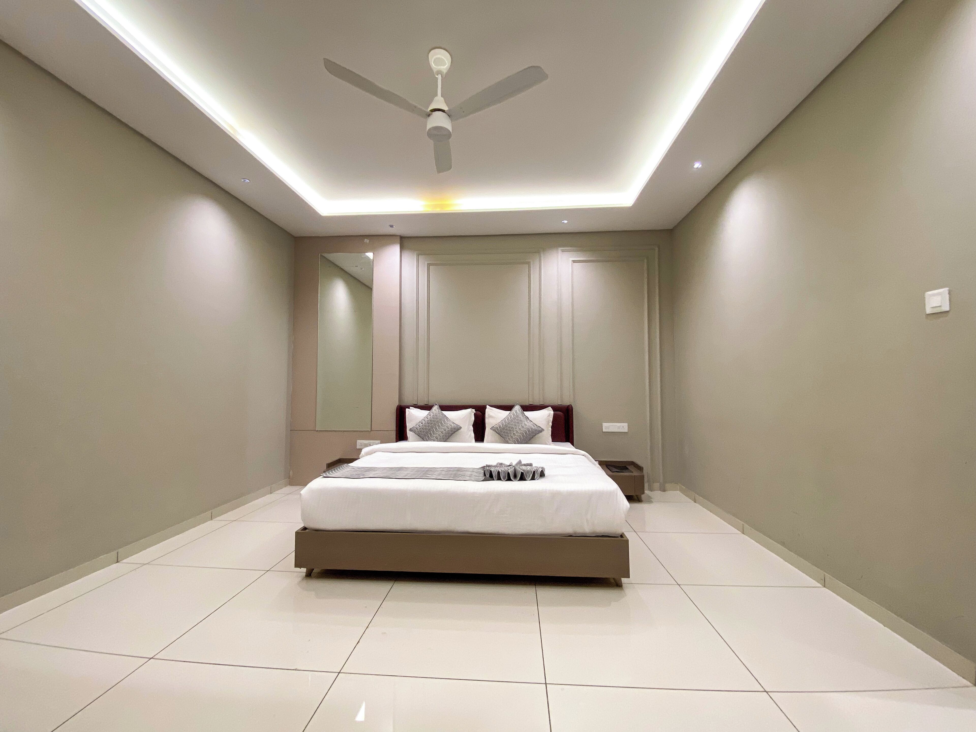 A modern bedroom with a bed centered in the room, a ceiling fan, and a large mirror on the wall.