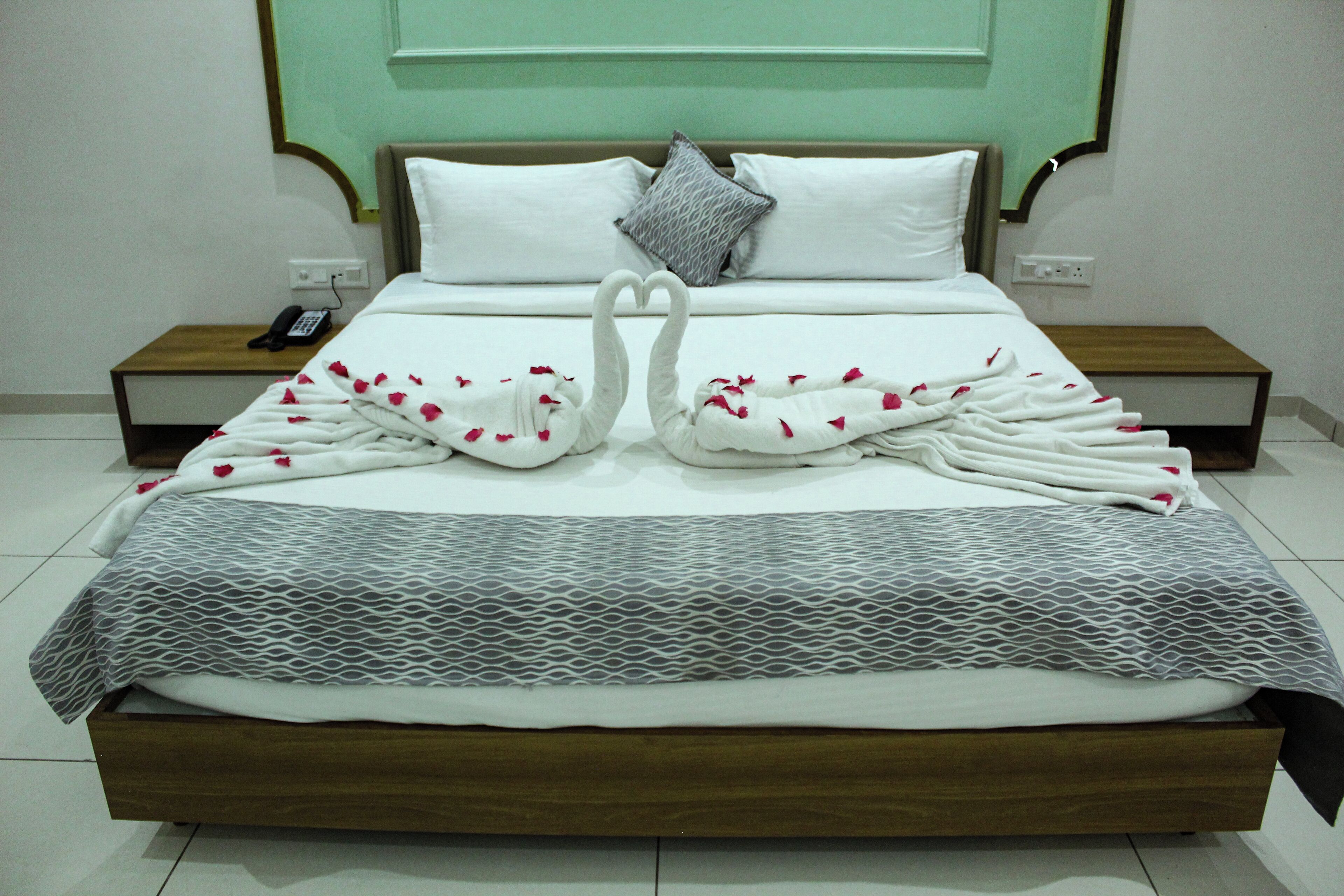 Una cama bien tendida con una toalla dispuesta en forma de cisne, una colcha estampada y una almohada con diseño geométrico.