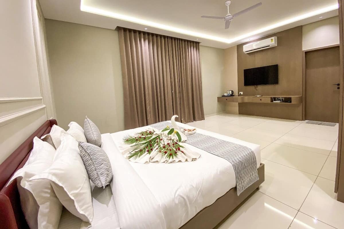 A hotel room with a large bed, a flat-screen TV, a ceiling fan, and a minibar.