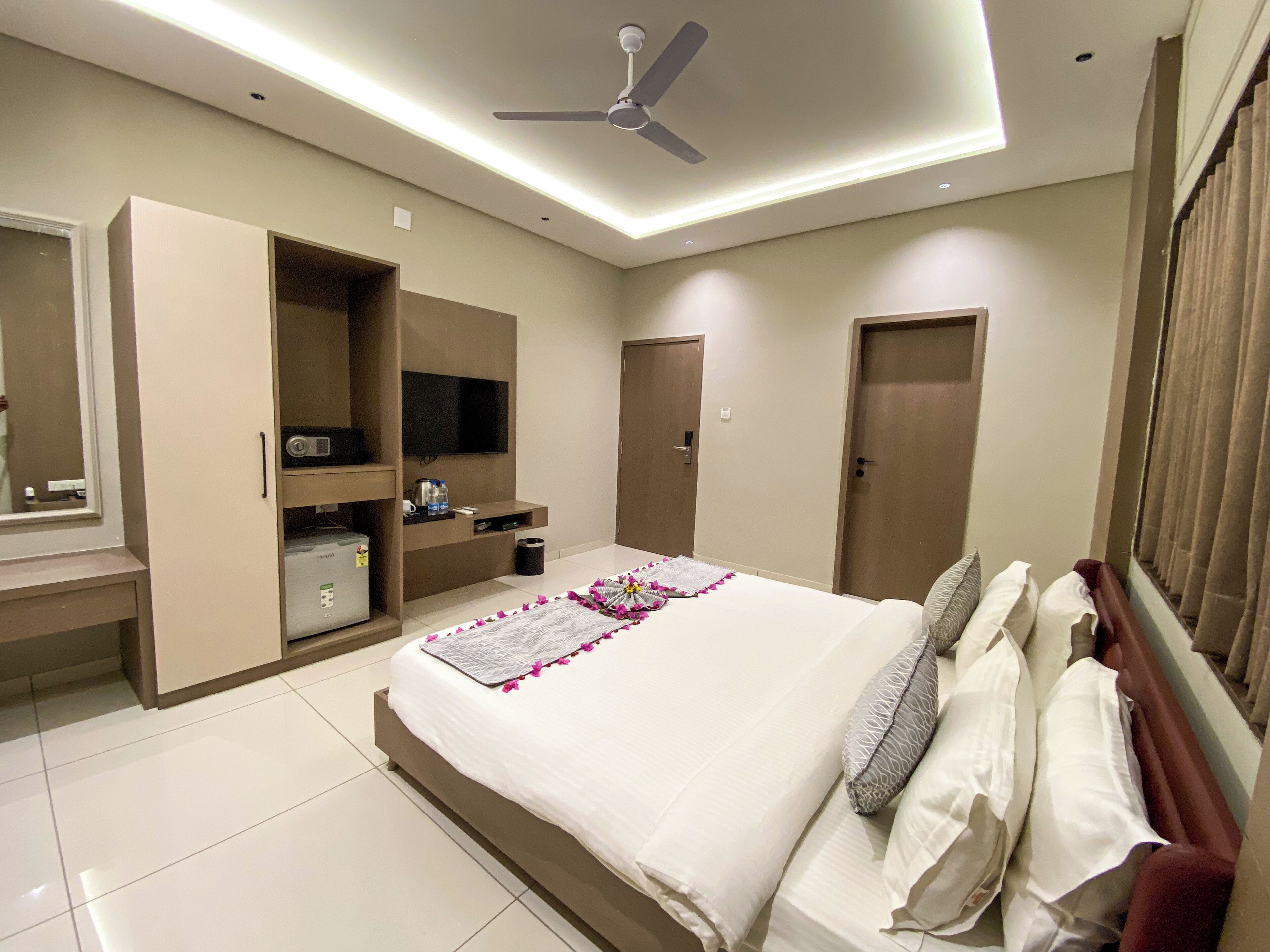 Una habitación de hotel moderna con una cama grande, un televisor, un armario y un ventilador de techo.