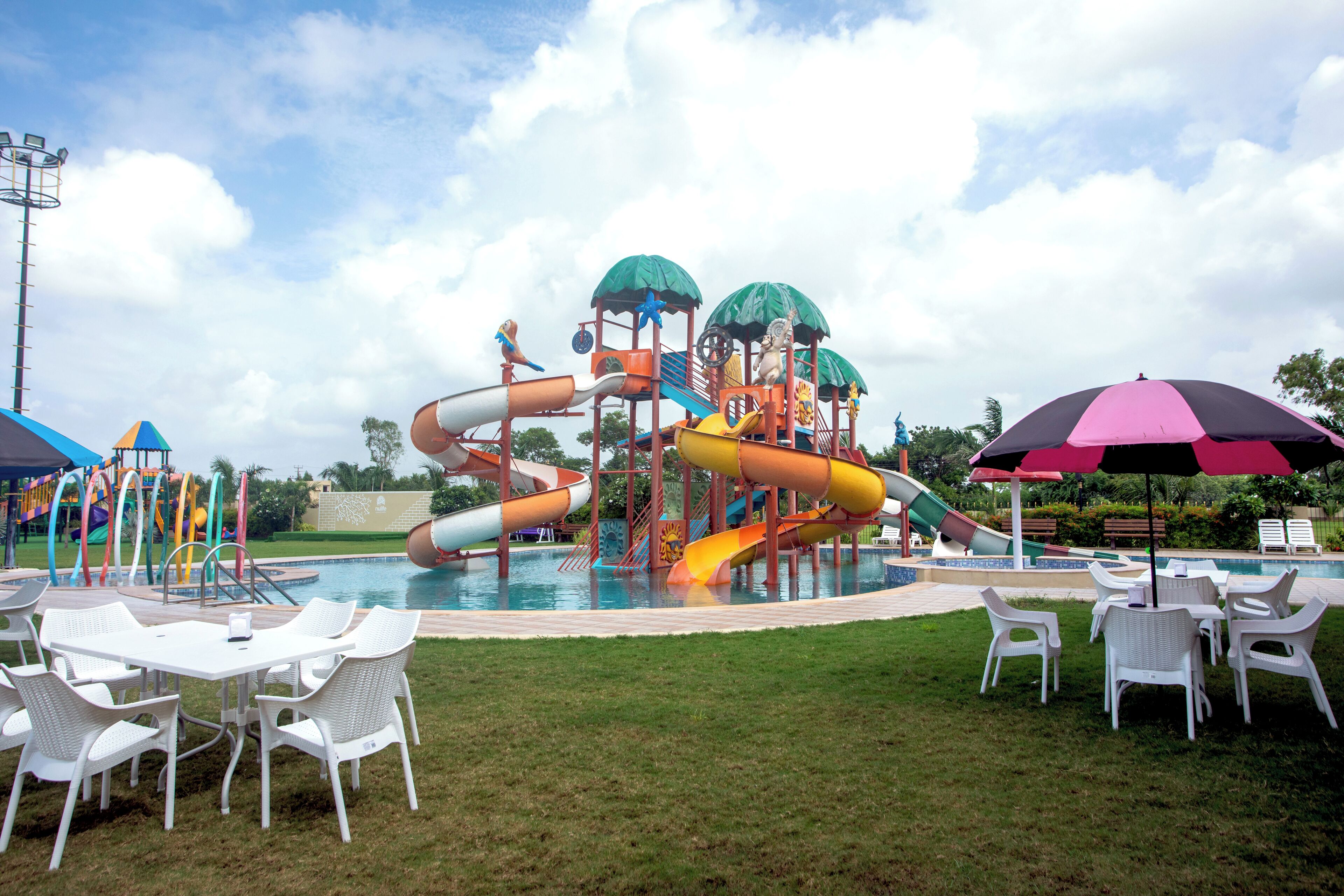 A water park with slides and play structures, surrounded by a pool and outdoor seating.