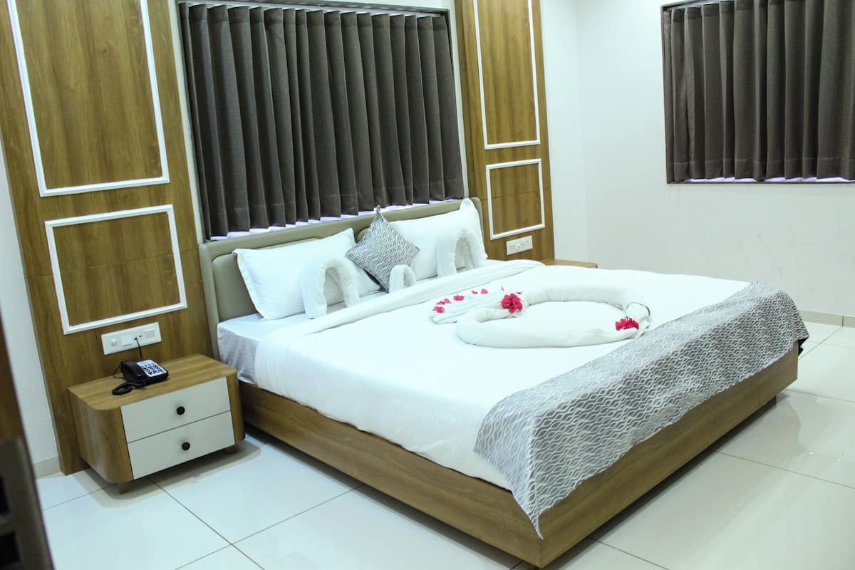 A neatly made bed with white linens, a bedside table with a phone, and a window with curtains.