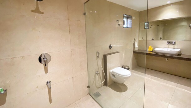 A modern bathroom with a glass shower enclosure, a toilet, and a sink with a mirror above. - nulife resort (Jamnagar)