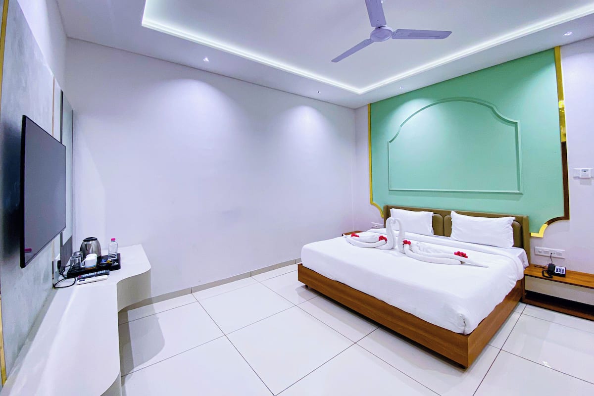 A modern hotel room with a large bed, a flat-screen TV, a bedside table with a coffee maker, and a ceiling fan.