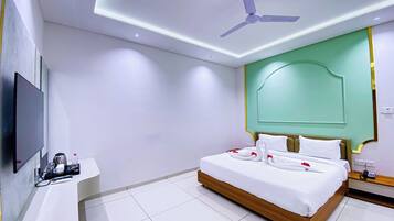 A modern hotel room with a large bed, a flat-screen TV, a bedside table with a coffee maker, and a ceiling fan.