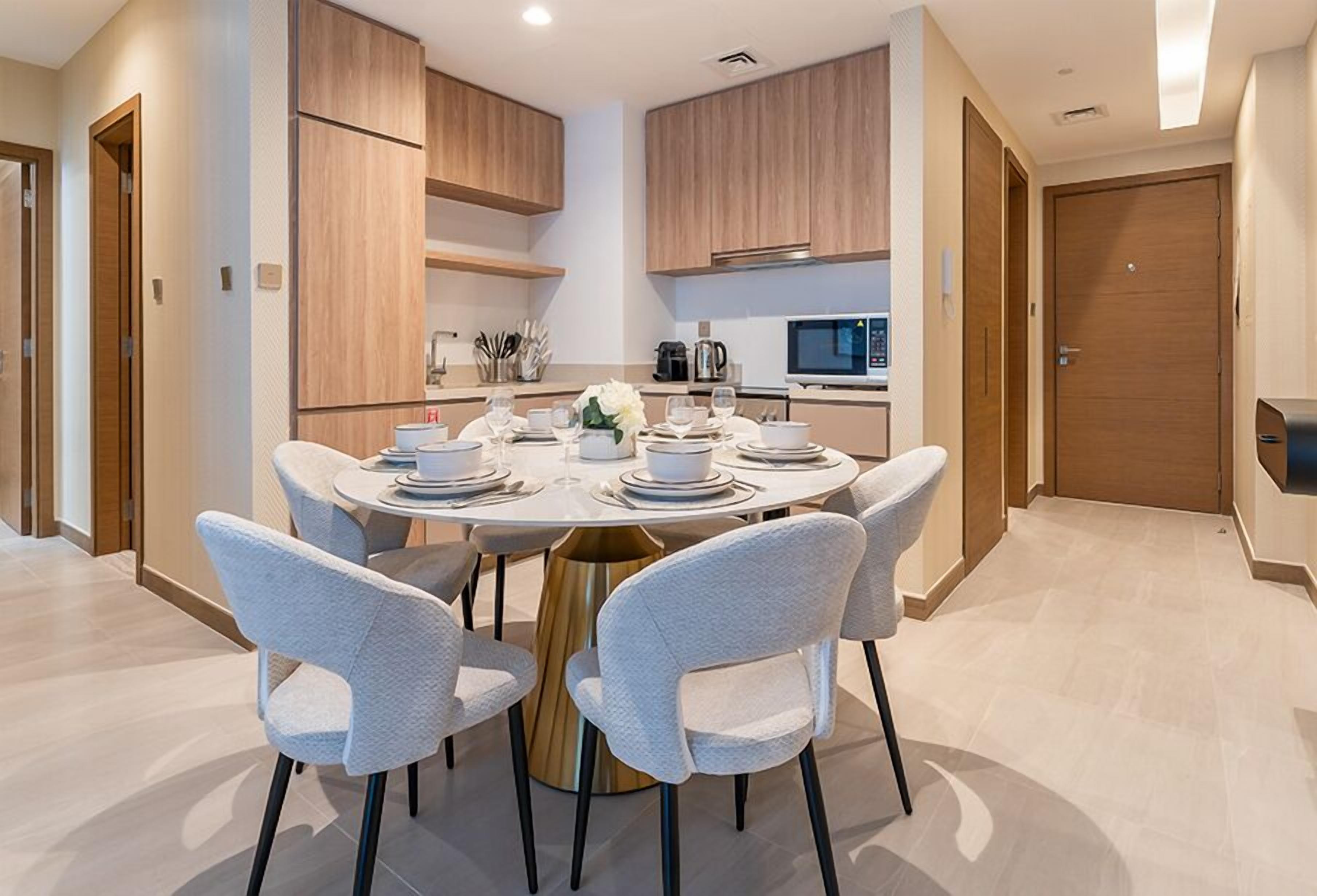 A modern kitchen with wooden cabinets, a round dining table with white chairs, and a built-in microwave.