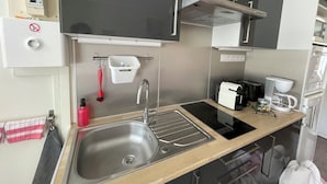 A modern kitchen with a stainless steel sink, a coffee machine, and a built-in oven. - Parvis Cathédrale Bayeux charming studio apartment (Bayeux)