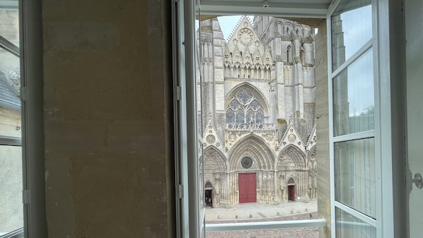 A view through a window of a Gothic-style building with intricate stonework and a red door. - Parvis Cathédrale Bayeux charming studio apartment (Bayeux)