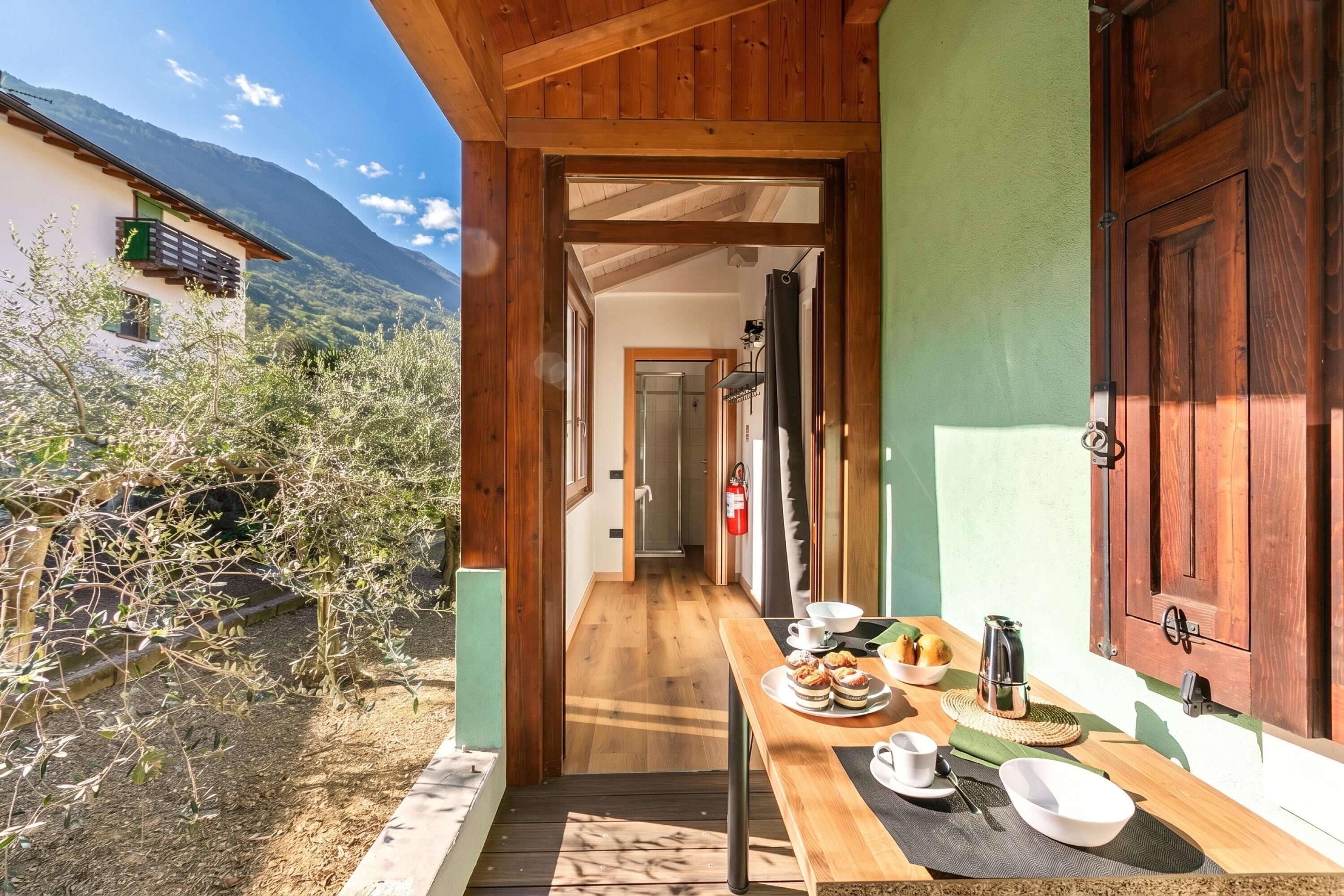 Une façade en bois abrite un espace repas avec une table dressée, où l’on peut admirer une vue sur la montagne, et une porte qui donne accès à une pièce.