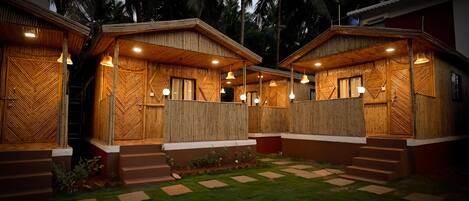 A wooden cabin-style building with a covered patio area, steps leading to the entrance, and a well-maintained lawn.