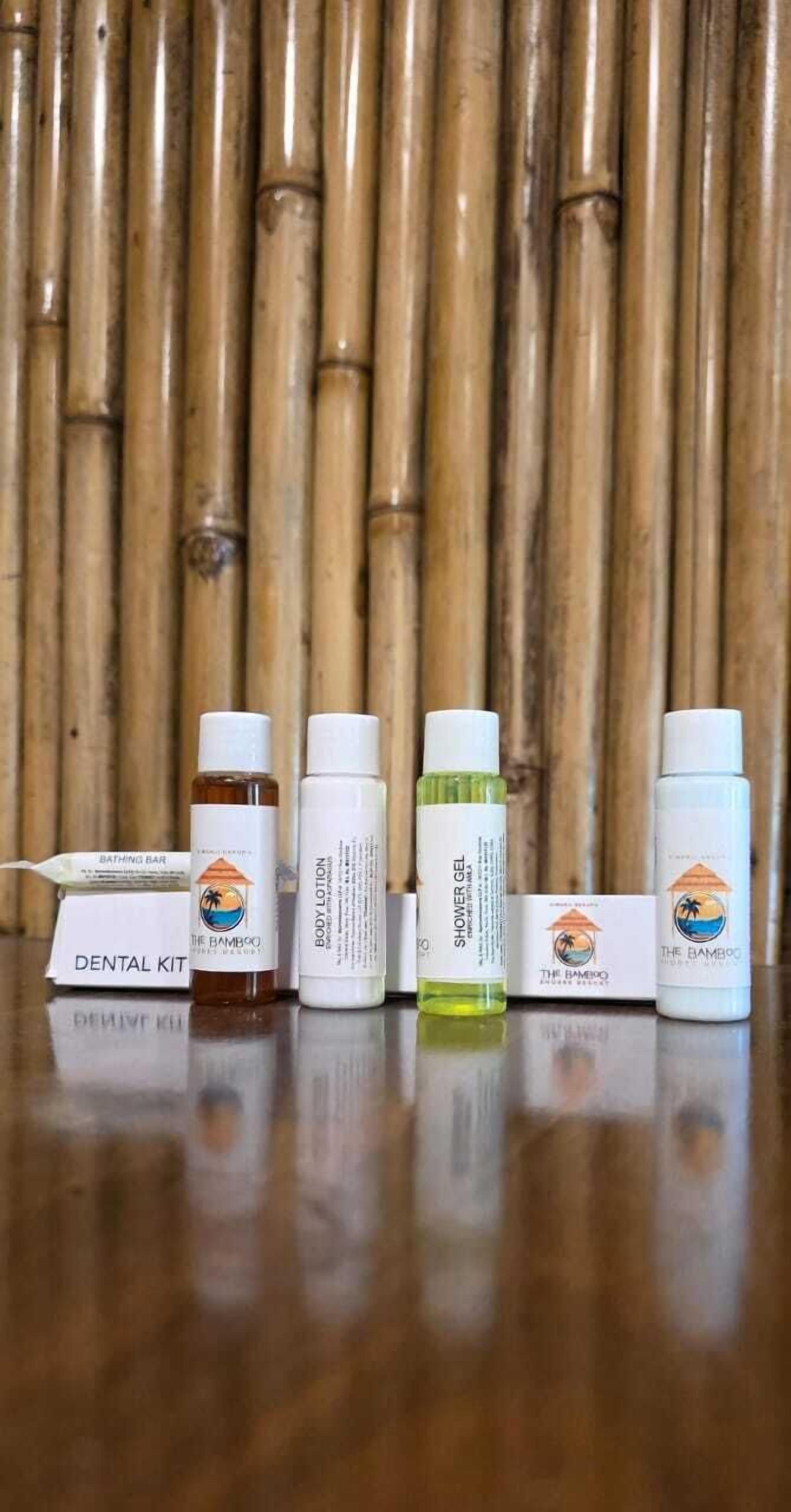 Une trousse de soins dentaires, une lotion pour le corps, un gel douche et deux bouteilles de shampoing, le tout posé sur une surface en bois avec un fond en bambou.
