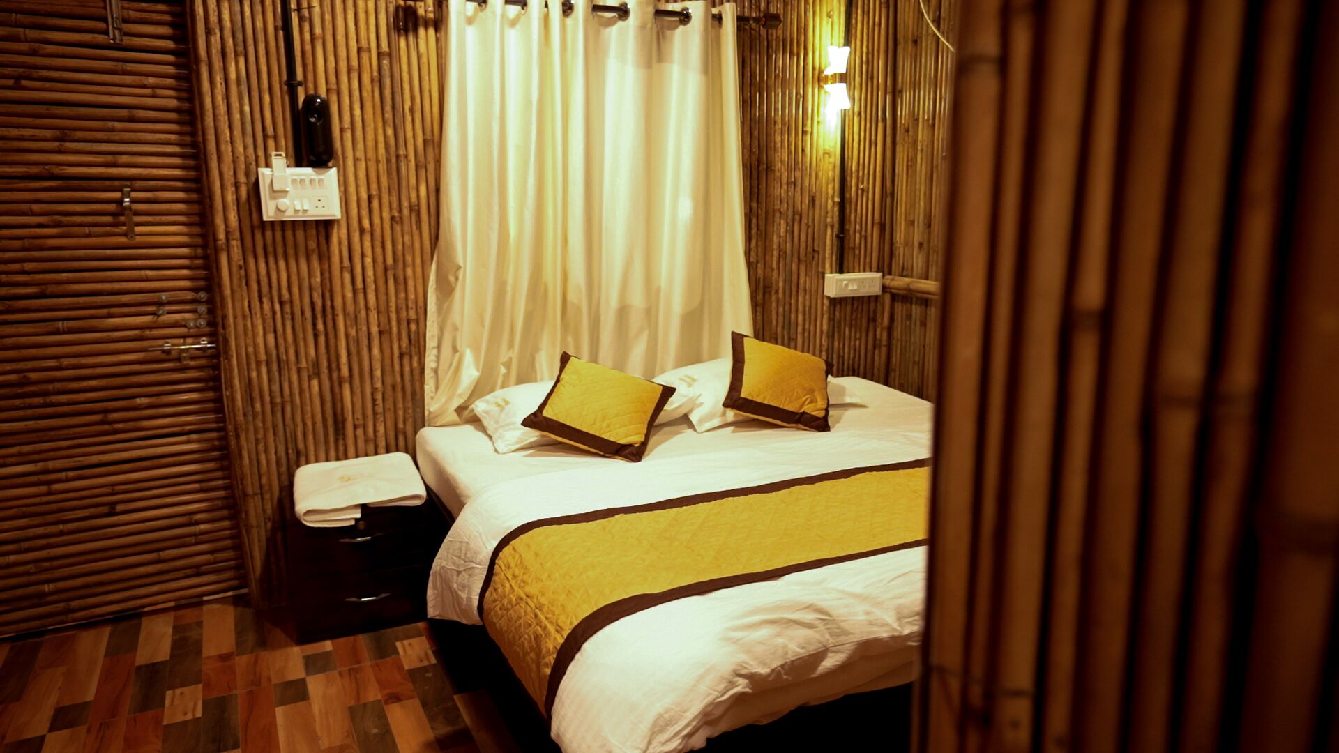 A room with a bed, a nightstand, a wooden floor, and a bamboo wall.