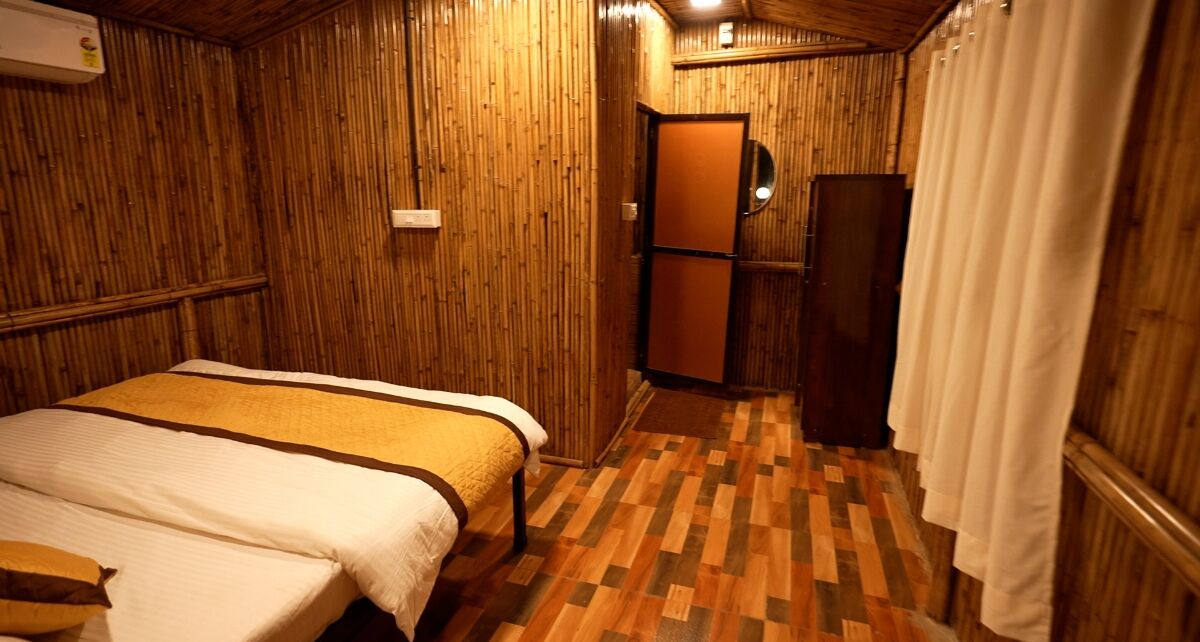 A small, cozy room with a bed, a wooden floor, and a door leading to a bathroom.