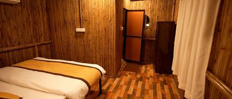 A small, cozy room with a bed, a wooden floor, and a door leading to a bathroom.