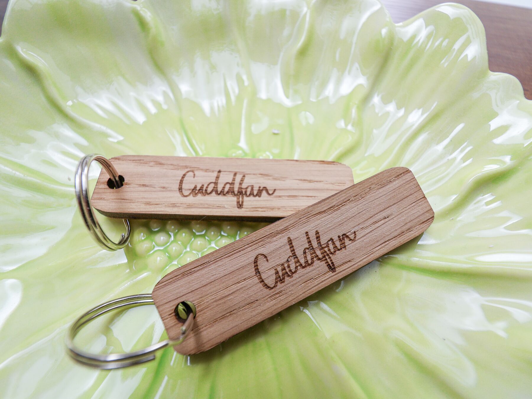Two wooden keychains with engraved names on a green, textured surface.