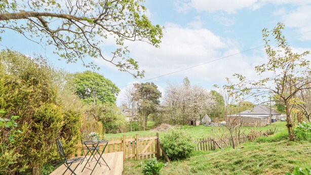 A wooden deck with a metal chair, surrounded by a wooden fence and lush greenery. - Cuddfan at Swallow Cottage (Mold)