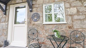 Ein Steinhaus mit einer weißen Tür, einem Fenster mit weißem Rahmen und drei Metallstühlen mit einem Tisch davor.
