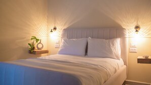 Un lit bien fait, avec du linge de lit blanc, deux tables de chevet avec des lampes et une plante en pot posée sur l’une des tables.