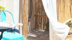 Une pergola en bois avec un rideau blanc, une douche suspendue et une petite table avec une chaise.