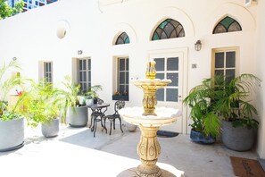 A courtyard with a central fountain, potted plants, outdoor seating, and a white building with arched windows and doors. - PORT CITY HAIFA - Urban Oasis (Haifa)