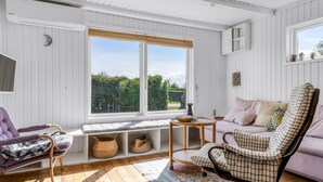Ein gemütliches Zimmer mit einem großen Fenster, einem violetten Sessel, einem karierten Stuhl und einem kleinen Tisch.