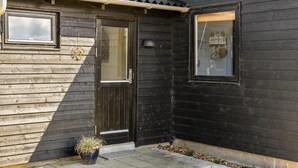 Ein Holzhaus mit einer dunklen Tür, einem kleinen Fenster und einem Blumentopf davor.