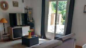 Un salon moderne avec un canapé, un téléviseur, une petite table avec une lampe et une vue sur l’extérieur grâce à une porte coulissante.