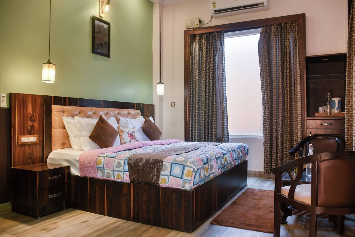 A bedroom with a wooden bed, bedside tables, a chair, a desk, and a window with curtains.