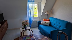 A room with a blue sofa, a wooden chair, a small table with a floral vase, and a lamp.