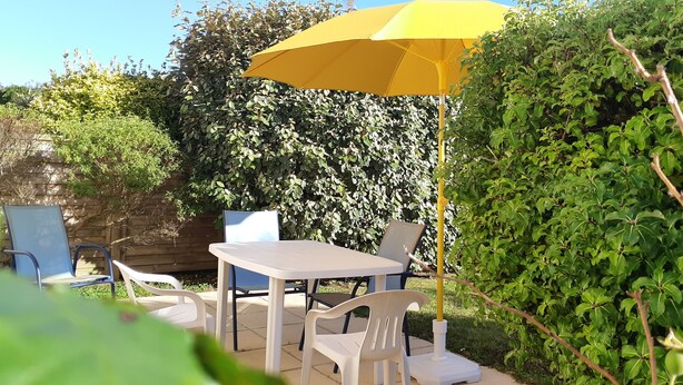 A patio with a table and chairs, a yellow umbrella, and lush greenery.