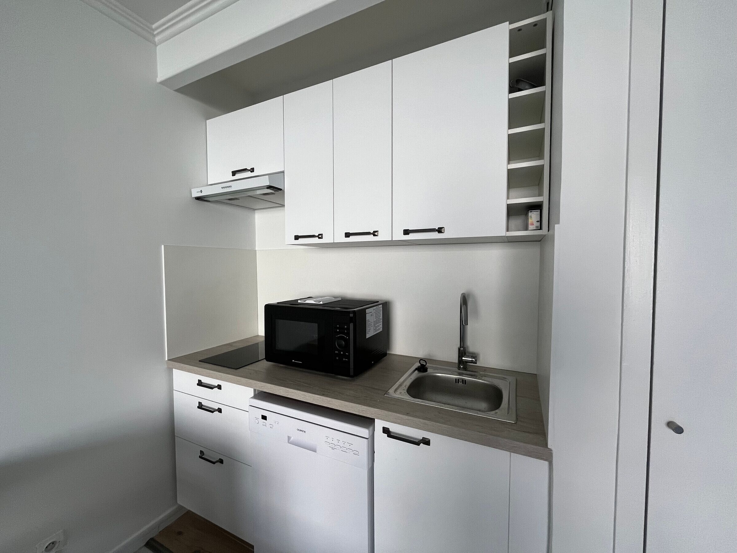 A compact kitchen with white cabinetry, a built-in microwave, a sink, and a dishwasher.