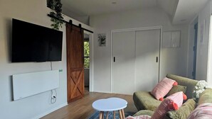 A living room with a large TV, a sliding door, a white sofa with cushions, and a small round table. - Relax and enjoy the North Shore in this cozy and stylish unit. (Auckland)
