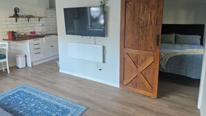 A modern living space with a kitchen area, a sliding barn door leading to a bedroom, and a mounted flat-screen TV. - Relax and enjoy the North Shore in this cozy and stylish unit. (Auckland)
