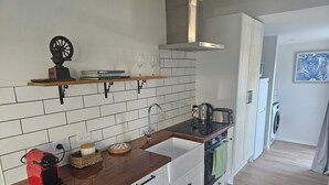 A modern kitchen with white cabinets, a wooden countertop, and a built-in oven. There is a coffee maker, a kettle, and a toaster on the counter. - Relax and enjoy the North Shore in this cozy and stylish unit. (Auckland)