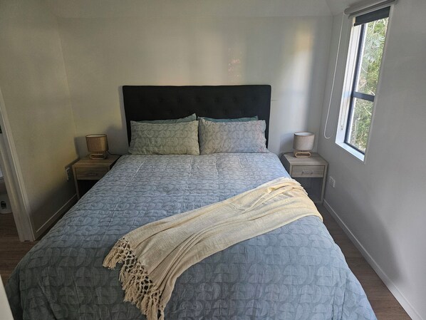 Un dormitorio con una cama, dos mesitas de noche, una ventana y vista a zonas verdes.