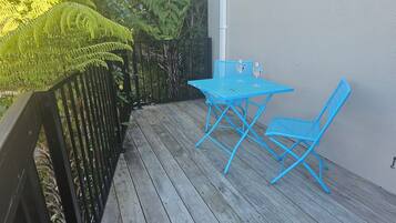 A wooden deck with a blue metal table and two chairs, surrounded by greenery and a black metal fence.