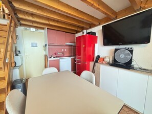 A compact kitchen with a dining area, wooden beams, a red refrigerator, and a mounted TV. - Saint-Cyprien - Duplex 2 bedrooms with terrace and private parking (Saint-Cyprien)