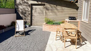 Une cabane en bois dotée d’un patio couvert, d’un jardinier en briques agrémenté de plantes et d’une table avec des chaises.