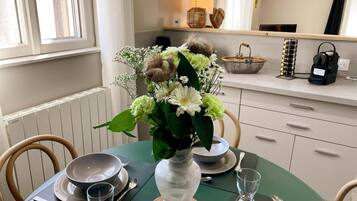 Et spisebord dækket med tallerkener, skåle og glas, en vase med blomster og et vindue med gardiner.