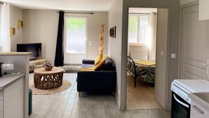 Un salon moderne comprenant un canapé, un téléviseur, un coin repas avec une table et des chaises, et un coin cuisine avec une cuisinière.