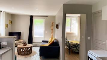 En moderne stue med sofa, TV, spiseplads med bord og stole samt et køkken med komfur.